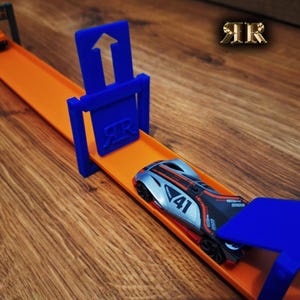 Op de afbeelding: Een blauwe en oranje Hot Wheels racebaan met een blauwe finishpoort en een zilveren auto met nummer 41.