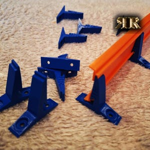 Op de afbeelding: Een set blauwe plastic baanondersteuningen voor een speelgoedracebaan. De ondersteuningen zijn ontworpen om de oranje baandelen vast te houden. Er zijn ook verschillende kleinere blauwe plastic onderdelen die worden gebruikt om de baandelen aan elkaar te verbinden.
