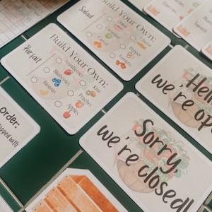 Pode incluir: Um conjunto de cartões imprimíveis para um mercado ou loja de brincar de faz de conta. Os cartões apresentam uma variedade de alimentos, incluindo salada, parfait, morangos, mirtilos, bananas, kiwi, pêssegos, maçãs, cebola, pepino, cenoura, pimenta, tomate e queijo. Os cartões também incluem uma placa que diz "Desculpe, estamos fechados!"