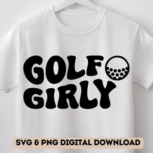 May include: White t-shirt with black text that reads "GOLF GIRLY" and a black golf ball graphic.
