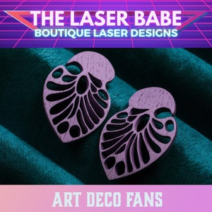 Puede incluir: Un par de pendientes de madera púrpura con un diseño de abanico art déco. Los pendientes están sobre un fondo de tela turquesa. El texto "Art Deco Fans" está en la parte inferior de la imagen.