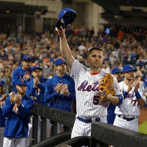 Puede incluir: Un jugador de béisbol con un uniforme a rayas azul y blanco levanta su gorra en el aire mientras sus compañeros de equipo lo animan. El jugador lleva un guante y tiene la palabra "Mets" en su camiseta.
