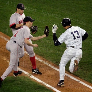 May include: Baseball game action shot featuring three players. Two players in gray uniforms with red accents and the word "BOS" on the chest. One player in a pinstripe uniform with the number 13. All are wearing baseball caps.