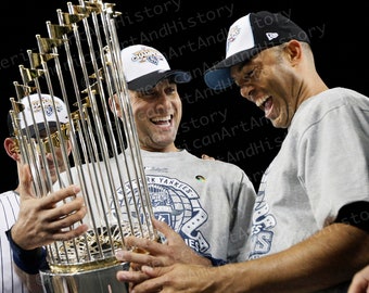 Puede incluir: Tres jugadores de béisbol sonriendo y sosteniendo un trofeo plateado con detalles dorados. El trofeo tiene las palabras "World Series" en él. Los jugadores llevan uniformes de béisbol con las palabras "New York Yankees" en ellos.