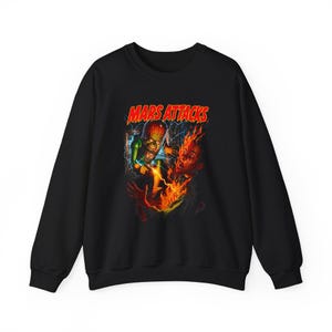May include: Black crewneck sweatshirt featuring a graphic from the movie "Mars Attacks." The graphic shows a Martian holding a ray gun, with flames and the movie title in red and yellow. The sweatshirt is made of a soft material.