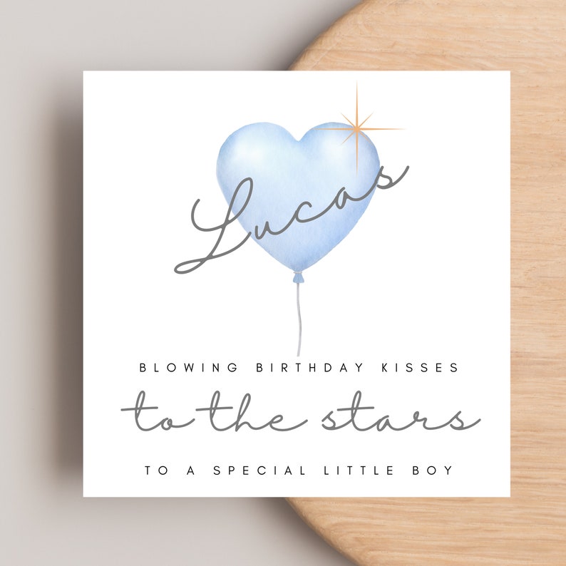 May include: A blue heart-shaped balloon with the name "Lucas" written in cursive script. The balloon has a gold star above it and is floating with a string. The text "Blowing birthday kisses to the stars" is written below the balloon. The text "To a special little boy" is written below the text.