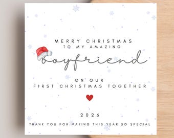 Könnte beinhalten: Eine quadratische Grußkarte mit weißem Hintergrund und hellblauen Schneeflocken. Der Text lautet: MERRY CHRISTMAS TO MY AMAZING boyfriend ON OUR FIRST CHRISTMAS TOGETHER, 2026, THANK YOU FOR MAKING THIS YEAR SO SPECIAL. Eine rote Weihnachtsmütze liegt auf dem Wort boyfriend und ein kleines rotes Herz befindet sich unter dem Text.