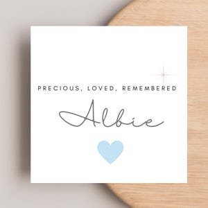 May include: A white card with the text "PRECIOUS, LOVED, REMEMBERED" above the name "Albie" in gray script. A light blue heart is below the name, and a starburst graphic is to the right.