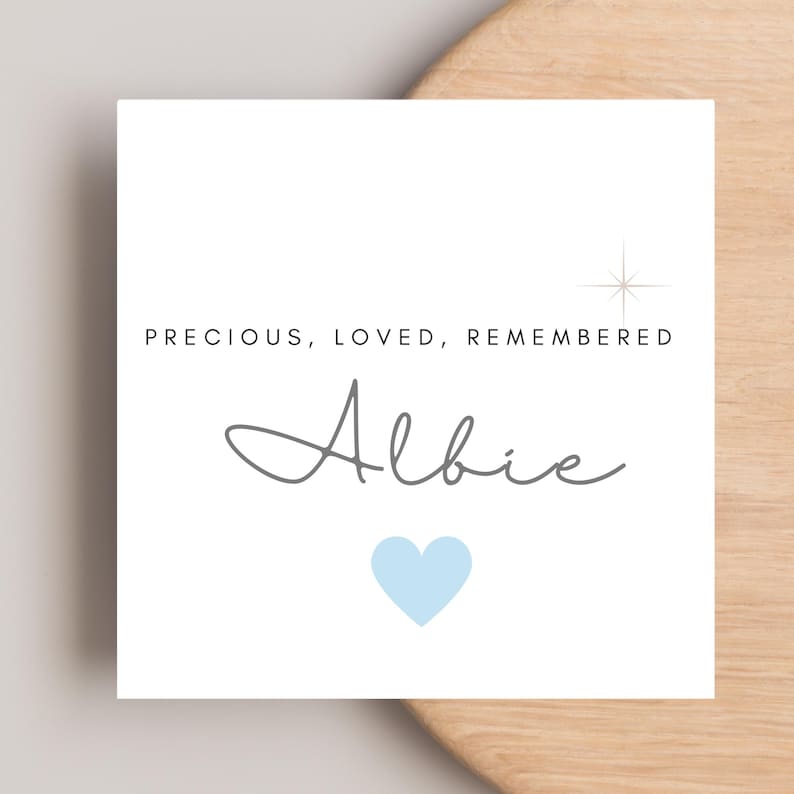 May include: A white card with the text "PRECIOUS, LOVED, REMEMBERED" above the name "Albie" in gray script. A light blue heart is below the name, and a starburst graphic is to the right.