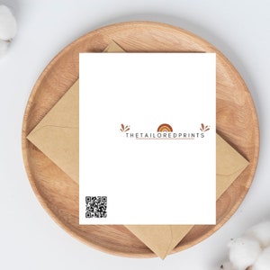 Op de afbeelding: Een witte kaart met een bruine envelop. De kaart heeft een QR-code en de tekst "THETAILOREDPRINTS" met een gestileerd regenboog- en bladontwerp.