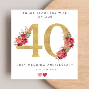 May include: A white card with gold glitter numbers "40" surrounded by red and pink watercolour flowers. The text "To my beautiful wife on our Ruby Wedding Anniversary 21st June 2023" is printed on the card.