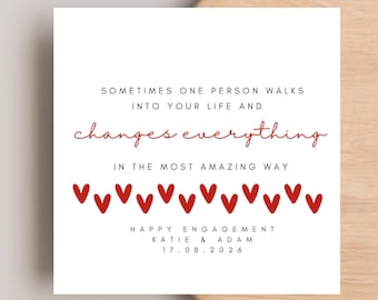 May include: A square white greeting card featuring black text that reads: SOMETIMES ONE PERSON WALKS INTO YOUR LIFE AND, followed by the red script text changes everything, and black text: IN THE MOST AMAZING WAY. Below are red hearts, HAPPY ENGAGEMENT, KATIE & ADAM, 17.08.2026.