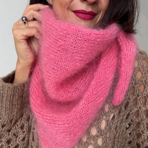 May include: A vibrant pink, fluffy scarf is draped around the neck. The scarf is made of a soft, fuzzy material. The person wearing the scarf is also wearing a brown sweater with a unique open knit design.