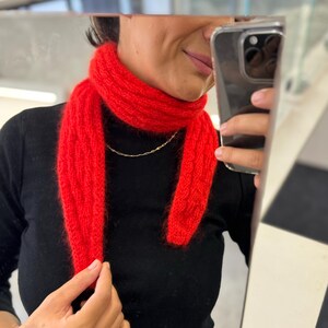 Könnte beinhalten: Ein roter Strick Schal mit einem Zopfmuster. Der Schal wird um den Hals einer Person getragen.