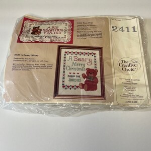 May include: A cross-stitch kit featuring a red and white bear with the text "A Beary Merry Christmas" and "From the Johnsons". The kit includes 14-count Aida cloth, cotton embroidery floss, a tapestry needle, a graph, an alphabet to personalize, and instructions. The finished size is 7" x 7".