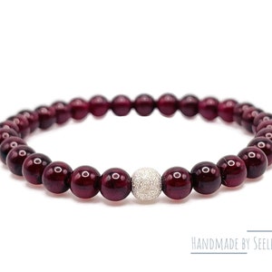 Könnte beinhalten: Ein Armband aus roten Edelsteinen mit einem silbernen Perlenakzent. Das Armband besteht aus kleinen, runden Perlen und hat ein schlichtes, elegantes Design.  Handgefertigt von Seelenwohl.