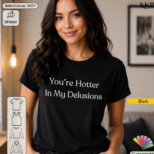 Op de afbeelding: Een zwart t-shirt met korte mouwen en de witte tekst "You're Hotter In My Delusions" op de voorzijde. Het kledingstuk heeft een ronde hals en een standaard pasvorm, gepresenteerd als een Bella+Canvas 3001 unisex model in de kleur zwart.