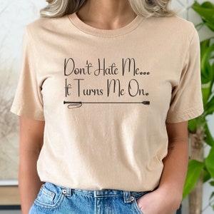 Könnte beinhalten: Ein beiges T-Shirt mit dem Text "Don't Hate Me... It Turns Me On." und einer schwarzen Peitschengrafik.