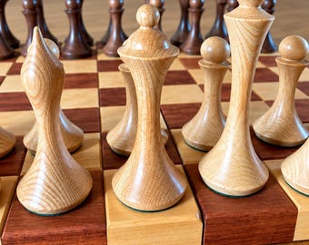 May include: A wooden chess set featuring light-colored pieces with visible grain patterns and dark-colored pieces arranged on a checkered board. The light pieces include a tall king, a queen, and pawns, while the dark pieces are positioned behind them.