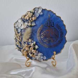 May include: A blue resin art piece with gold accents and dried flowers. The piece features Arabic calligraphy and is displayed on a gold stand.