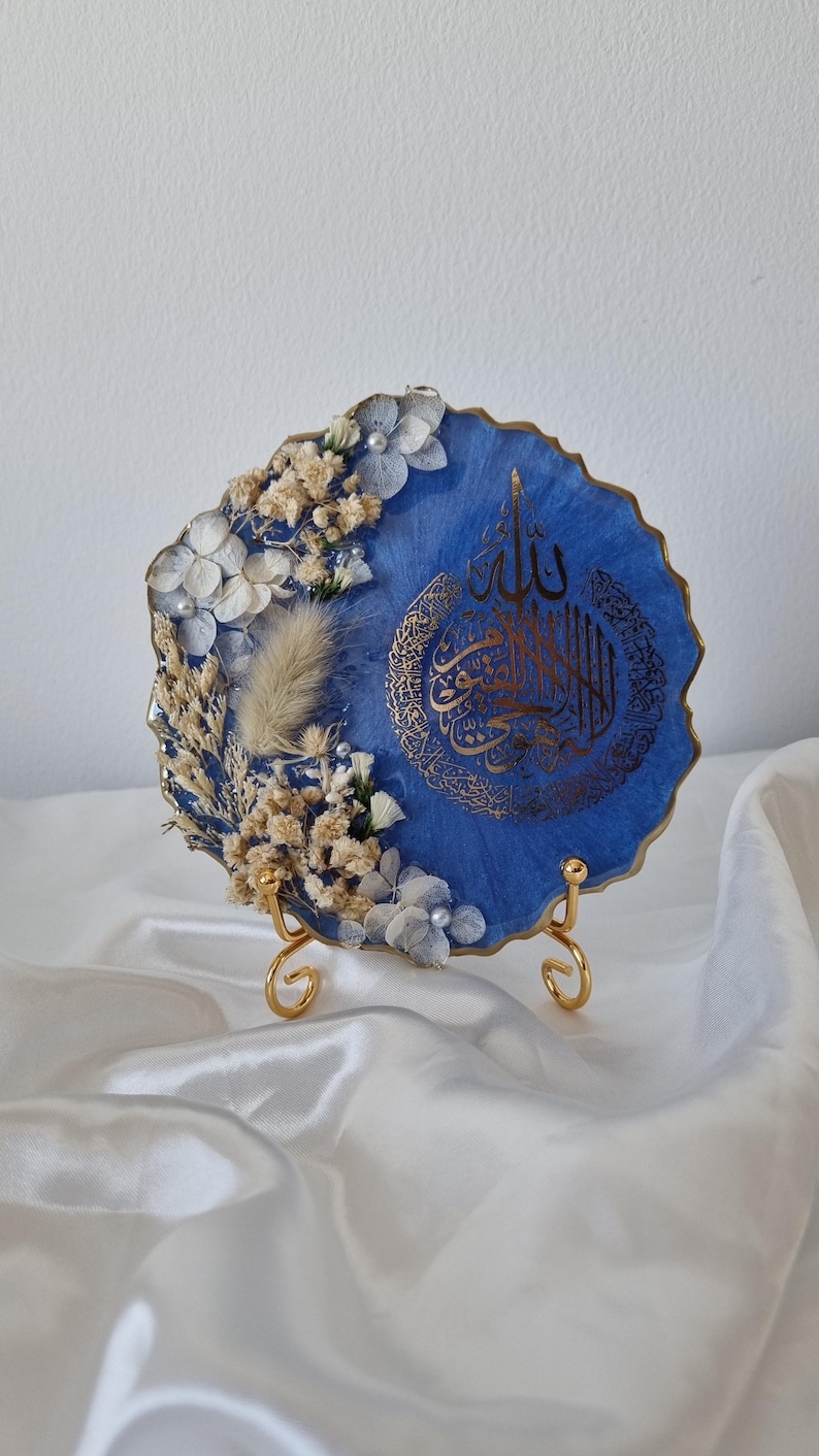 May include: A blue resin art piece with gold accents and dried flowers. The piece features Arabic calligraphy and is displayed on a gold stand.