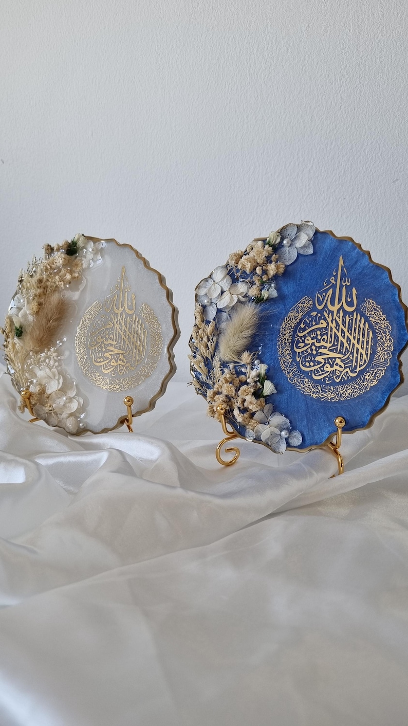 May include: Two round resin art pieces with gold calligraphy and dried flowers. The pieces are on gold metal stands and are displayed on a white surface.