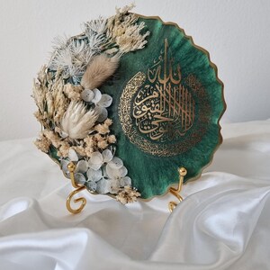 May include: A green resin plate with gold calligraphy and dried white flowers. The plate is on a gold stand.