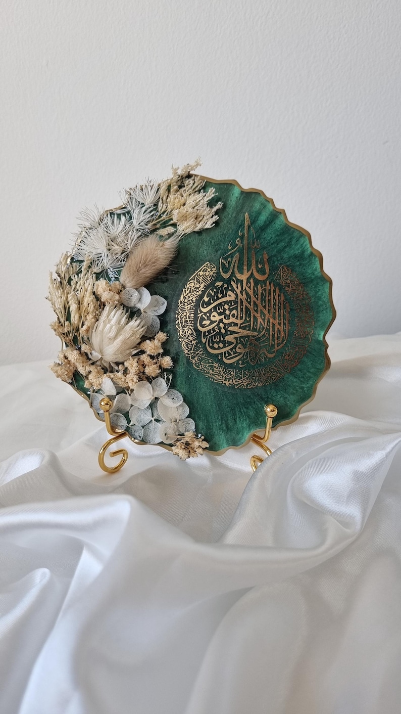 May include: A green resin plate with gold calligraphy and dried white flowers. The plate is on a gold stand.