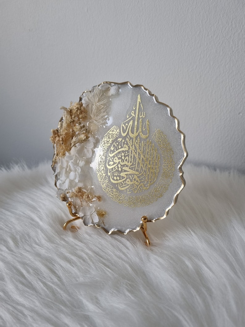 May include: White resin round tray with a gold metallic finish. The tray features a gold Arabic calligraphy design and dried flowers. The tray is on a gold metal stand.