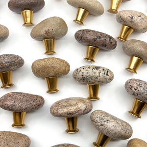 Könnte beinhalten: Eine Sammlung von 20 naturfarbenen Steinknaufgriffen mit goldfarbener Metallbeschläge. Die Knäufe sind in verschiedenen Formen und Größen, mit einer Mischung aus braunen, grauen und weißen Tönen.