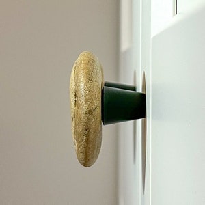 Könnte beinhalten: Nahaufnahme einer Holztür mit einem runden, hellbraunen Knopf und einem schwarzen Metallstiel. Die Schranktür ist weiß.