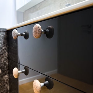 May include: Close-up of black cabinet drawers with stone-shaped knobs. The knobs are a light brown colour with darker brown speckles.