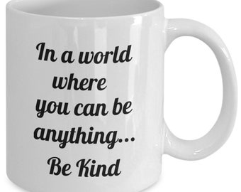 May include: White ceramic coffee mug with black text that reads "In a world where you can be anything... Be Kind."