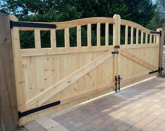 May include: A pair of wooden double gates with a curved top and black metal hinges. The gates are closed and are in front of a brick driveway.