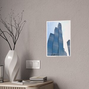 May include: A photograph of a tall, modern skyscraper with a glass facade. The building is reflected in the glass of the surrounding buildings. The sky is blue and there are clouds in the distance.