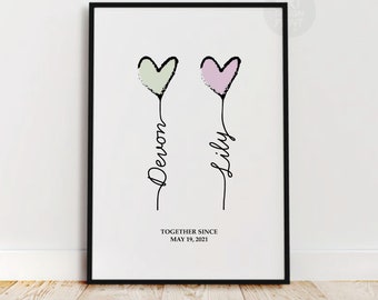 Può includere: Una stampa incorniciata nera con due cuori in diverse tonalità di rosa e verde. I cuori sono collegati da stringhe con i nomi Devon e Lily scritti su di essi. Il testo "Together Since May 19, 2021" è in fondo alla stampa.