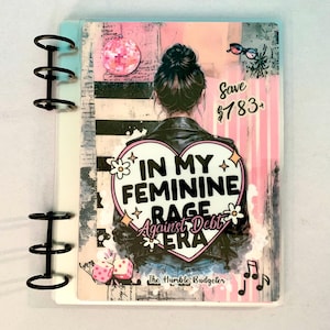 May include: A planner with a pink and black design. The cover features an illustration of a woman in a leather jacket with the text "IN MY FEMININE RAGE AGAINST DEBT ERA". Additional text includes "Save $783+" and "The Humble Budgeter".