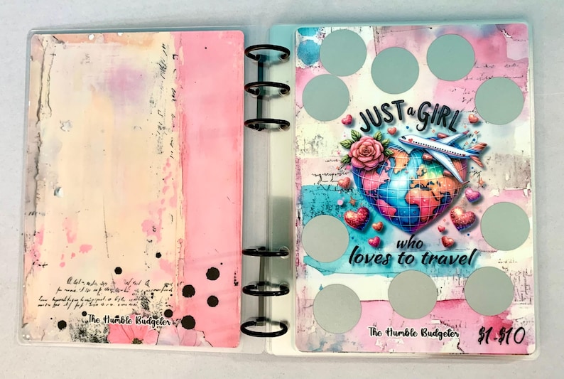 May include: A clear binder with a pink and cream abstract design on the left and a travel-themed design on the right. The right side features a globe, airplane, hearts, and the text "JUST a GIRL who loves to travel."