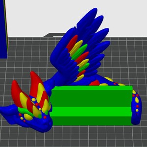 May include: A blue, red, yellow, and green 3D printed dragon phone stand. The dragon has wings and a colorful, spotted body. The stand has two slots for phones.