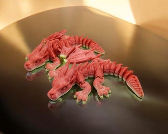 May include: Two red watermelon dragon sculptures on a silver surface. The dragons are carved with intricate details and have a realistic appearance.