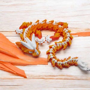 May include: A bright orange and white dragon made of food, possibly carrots, is curled up on a wooden surface.