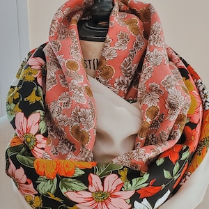 Pode incluir: Uma echarpe reversível com estampa floral. Um lado é preto com flores rosa, laranja e amarelas. O outro lado é rosa com desenhos florais marrons e brancos.