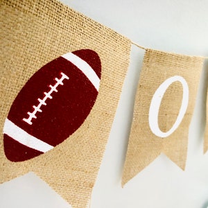 May include: A burlap banner with the word "ONE" in white letters and a red and white football on one of the flags.