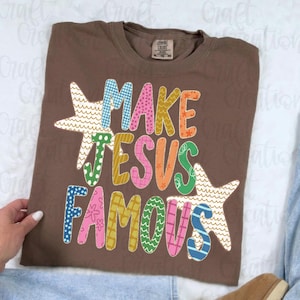 May include: A brown short-sleeve t-shirt featuring the text "MAKE JESUS FAMOUS" in large, multi-coloured, patterned letters. The design includes two large starfish graphics integrated with the text, which features various patterns like dots, waves, and grids in shades of blue, pink, green, orange, and yellow.