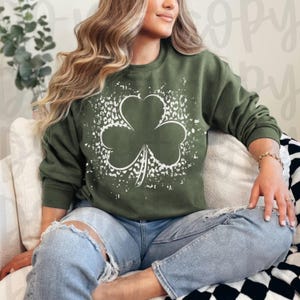 Puede incluir: Una sudadera verde con un diseño de trébol blanco. El trébol está rodeado de un patrón de leopardo blanco.