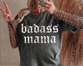 May include: A dark gray t-shirt with the text "badass mama" printed in white on the front. The text is in a gothic font style.