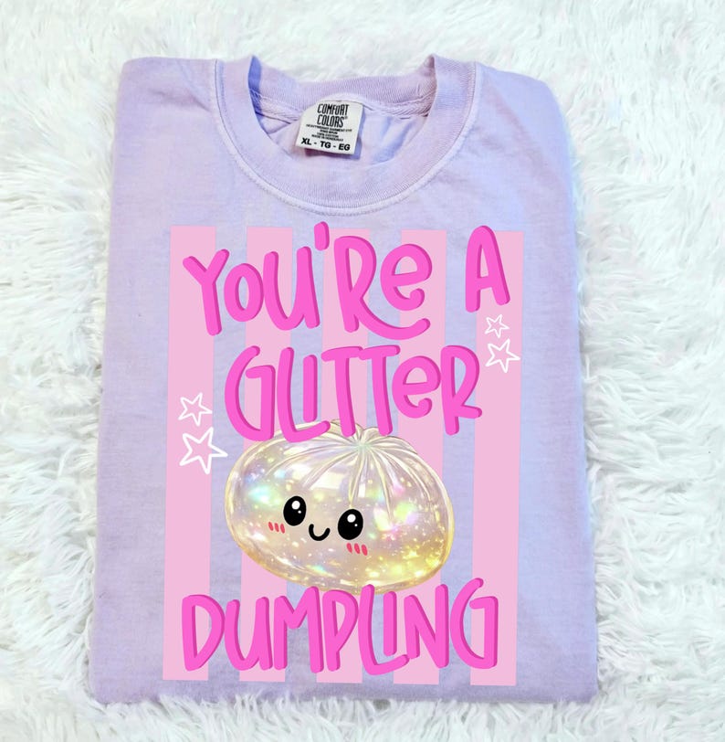May include: A light purple Comfort Colors XL-TG-EG sweatshirt. The front features a graphic with the text "You're a Glitter Dumpling." The graphic includes a cute, glittery dumpling with a smiling face, set against pink stripes and stars.