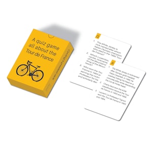 Op de afbeelding: Een gele quizspeldoos met de tekst "A quiz game all about the Tour de France" en een fietsafbeelding. Twee witte quizkaarten met vragen en antwoorden liggen naast de doos. De tekst "Cycling's greatest race" staat op de zijkant van de doos.