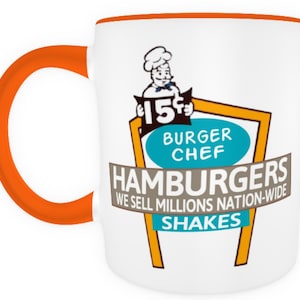 May include: White ceramic mug with an orange rim and handle. The mug features a vintage-style illustration of a chef holding a sign that reads "15¢ Burger Chef Hamburgers We Sell Millions Nation-Wide Shakes".