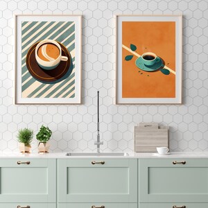 May include: Two framed prints of coffee cups. The first print features a blue and white striped background with a brown coffee cup with a white swirl of cream. The second print features an orange background with a green coffee cup on a green saucer.